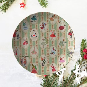 Könnte beinhalten: Ein runder, grün-weißer Keramikteller mit einem Vintage-Weihnachtsdesign. Der Teller zeigt ein sich wiederholendes Muster von Frauen in Kleidern und festlichen Dekorationen.