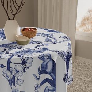 May include: A white round tablecloth with a blue and white floral and animal print. The tablecloth features monkeys, leopards, and flowers.