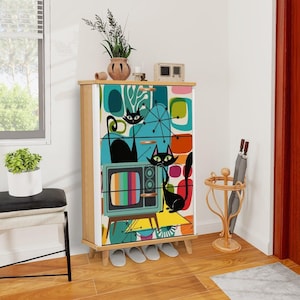 May include: A mid-century modern style cabinet with four drawers features a colorful graphic design of two black cats, a retro television, and abstract shapes in shades of blue, green, orange, and yellow.
