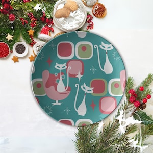 Könnte beinhalten: Ein tealblauer Keramik-Dinnerteller mit einem Retro-Design mit weißen Katzen, pinken und grünen geometrischen Formen und weißen Sternen.