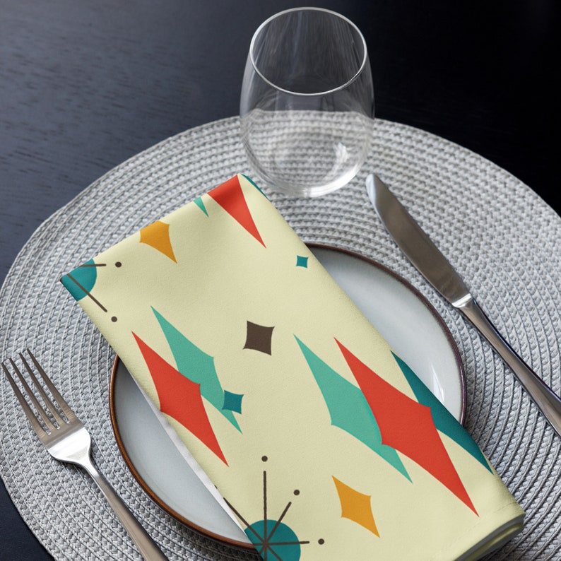 May include: A yellow, red, blue, and brown geometric patterned napkin on a gray placemat with a clear glass and a silver fork.