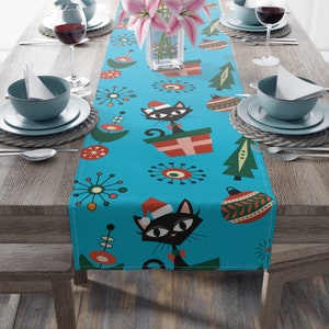 May include: A turquoise blue table runner with a repeating pattern of black cats wearing Santa hats, Christmas trees, ornaments, and abstract mid-century modern designs.