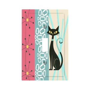 May include: A decorative light switch cover with a retro design. The cover features a black cat with yellow eyes, a teal collar, and a curled tail. The background has pink, teal, and cream-colored stripes with geometric shapes and starburst patterns.