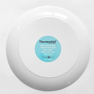 May include: White ceramic plate with a blue and white sticker that says "ThermoSaf" and lists the plate as microwave, dishwasher, and oven safe. The sticker also says "Melamine Free" and "BPA Free".