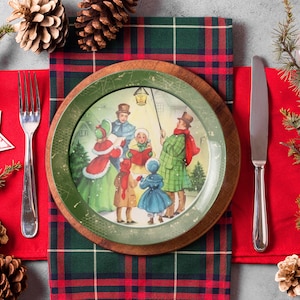 May include: A Christmas-themed dinner plate with a green and white design featuring a scene of carolers singing in a snowy village. The plate is set on a red and green plaid tablecloth with a silver fork and knife.