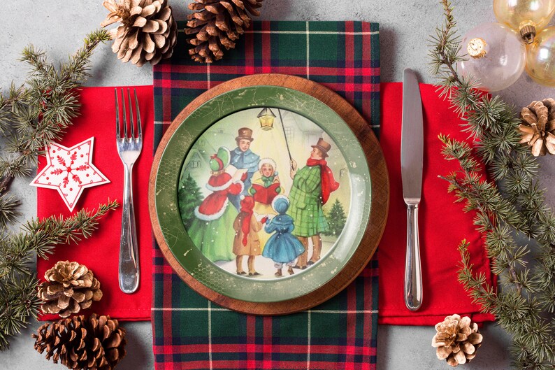 May include: A Christmas-themed dinner plate with a green and white design featuring a scene of carolers singing in a snowy village. The plate is set on a red and green plaid tablecloth with a silver fork and knife.