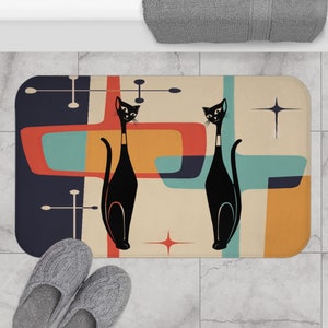 May include: A retro-style bath mat with a beige background and abstract shapes in shades of blue, orange, and red. Two black cats are standing on the mat, facing forward. The mat has a non-slip backing.