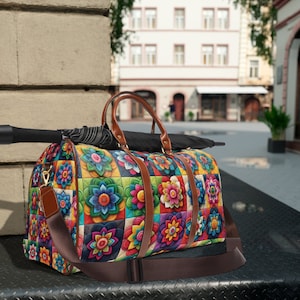 May include: A colorful duffel bag with a floral pattern. The bag features a repeating design of vibrant flowers in squares, with brown leather handles and a shoulder strap. An umbrella rests on top of the bag.