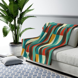 May include: A colourful throw blanket with a geometric pattern of wavy stripes in shades of brown, teal, orange, and cream. The blanket is draped over a white sofa.