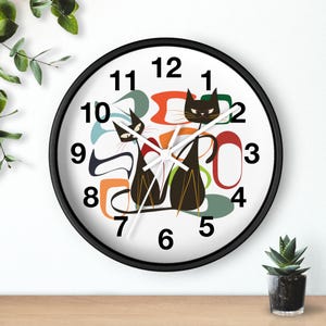 May include: A black and white wall clock with a retro design featuring two black cats and colorful abstract shapes. The clock face has black numbers and white hands.