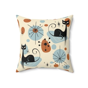 May include: A cream-colored throw pillow with a mid-century modern design featuring black cats, blue and orange abstract shapes, and starbursts.