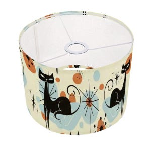 May include: A cream-colored lampshade with a black and white mid-century modern design featuring two black cats and abstract shapes in orange, blue, and white.
