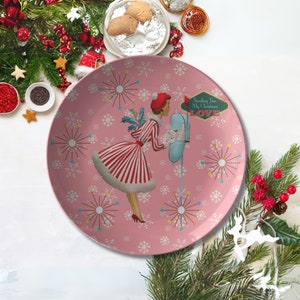 Könnte beinhalten: Rosa Keramikplatte mit einem Retro-Weihnachtsdesign, das eine Frau in einem rot-weiß gestreiften Kleid zeigt, die neben einem Briefkasten steht. Die Platte hat ein Schneeflocken- und Sternburst-Muster und den Text "Sending You My Christmas Love".