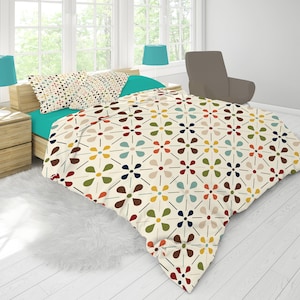 May include: A bed with a cream-colored comforter featuring a repeating floral pattern in red, brown, yellow, blue, and green. The bed has a teal sheet set and matching pillowcases. Two teal lamps sit on wooden nightstands.