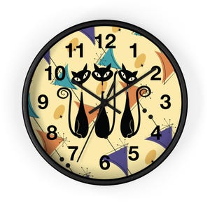 May include: A yellow and cream colored wall clock with black numbers and hands. The clock face features a retro design with three black cats and a pattern of blue, orange, and yellow geometric shapes.