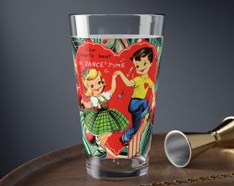 Puede incluir: Un vaso de vidrio transparente con un diseño vintage de San Valentín que presenta a un niño y una niña bailando. El diseño incluye el texto "Our hearts beat in dance time".