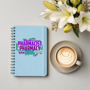Puede incluir: Un cuaderno azul claro con espiral con las palabras "Farmacéutico", "Farmacia" y "Medicamento" en un diseño de nube de palabras. Una taza de café con arte latte y un ramo de lirios blancos también están presentes.