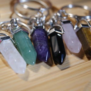 May include: Seven crystal point keychains with silver rings. The crystals are clear, green, purple, black, pink, and brown.