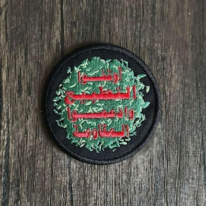 Op de afbeelding: Een geborduurde zwarte en groene patch met Arabische tekst in rood. De tekst luidt "لا إله إلا الله محمد رسول الله".