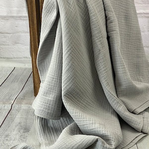 May include: A light gray, textured blanket draped over a wooden crate. The blanket has a crinkled appearance and a soft, flowing drape. The fabric appears to be a lightweight cotton or similar material, perfect for a cozy home decor.