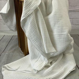 May include: A white, textured blanket draped over a wooden crate. The blanket has a crinkled appearance, with visible ridges and folds. The fabric appears soft and lightweight, suggesting a cozy textile.