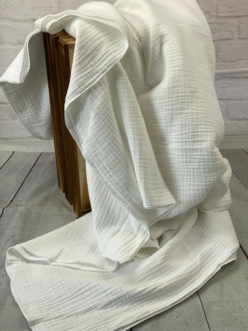 May include: A white, textured blanket draped over a wooden crate. The blanket has a crinkled appearance, with visible ridges and folds. The fabric appears soft and lightweight, suggesting a cozy textile.