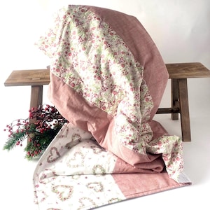 Könnte beinhalten: Eine Steppdecke mit einem einfarbigen, altrosa Stoffpaneel und einem weißen Paneel mit einem Blumenmuster aus kleinen roten Blüten und grünen Blättern. Der untere Teil zeigt einen weißen Stoff mit einem wiederkehrenden Muster aus herzförmigen Kränzen.