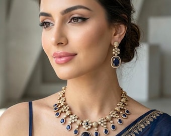 May include: A gold-toned necklace and matching drop earrings featuring oval-shaped deep blue stones surrounded by small white accents. The necklace has a central large blue stone with smaller dangling blue stones and textured gold metal links.