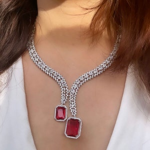 Può includere: Una collana d'argento con un designo a catena a strati e due ciondoli pendenti in pietra preziosa rossa. La collana è realizzata con pietre di zircone cubico.