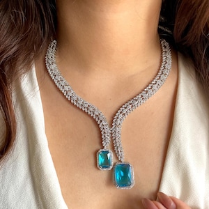 May include: A silver-toned necklace with two large, rectangular, light blue gemstones. The necklace has a delicate, intricate design with small, clear stones. The gemstones are set in a silver frame, creating a striking contrast.