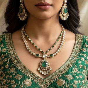 Pode incluir: Uma mulher usando um colar de ouro e brincos combinando com detalhes em esmeralda e diamante. O colar tem um grande pingente de esmeralda. A mulher está usando um top verde bordado.