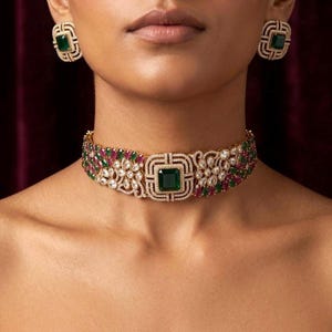 May include: A gold-toned choker necklace featuring a central square emerald-cut green stone surrounded by clear crystals, accented with alternating red and green stones in a floral pattern, paired with matching rectangular emerald-cut stud earrings.