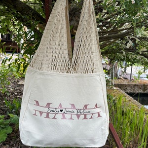 Könnte beinhalten: Eine weiße Canvas-Tragetasche mit braunem Netz oben. Die Tasche hat das Wort "MAMA" in Pink auf der Vorderseite aufgedruckt, darunter stehen die Namen "Emily, Leonie, Philina".