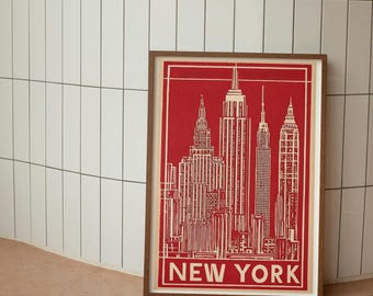May include: A framed rectangular print featuring a red and white graphic illustration of the New York City skyline. The artwork displays detailed line drawings of skyscrapers and the text NEW YORK in bold white capital letters at the bottom.