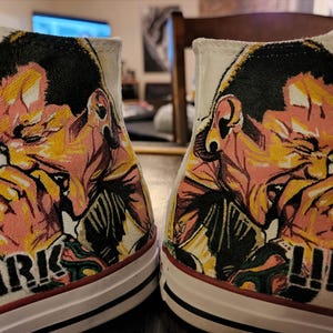 May include: A white ceramic mug with a black handle and the text "But First, Coffee" in a handwritten style. The mug is on a white surface. The mug is approximately 4 inches tall.