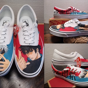 May include: White Vans Era sneakers customized with anime character artwork. The shoes feature red and blue accents, with detailed illustrations of anime characters on the sides. The laces are white, and the soles are white with a black stripe.