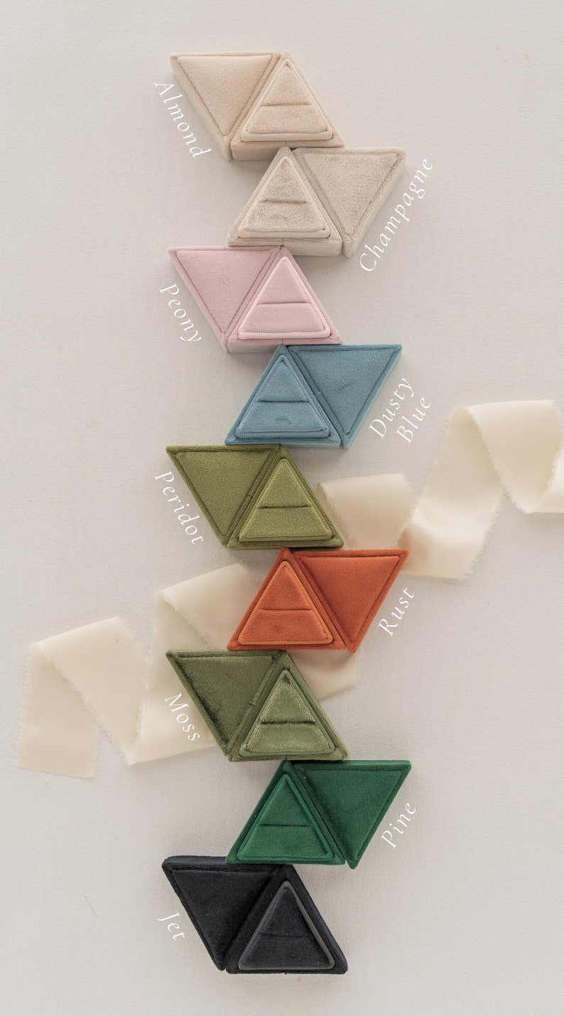 May include: Nine triangular ring boxes in a variety of colours, including almond, champagne, peony, dusty blue, peridot, rust, moss, pine, and jet. Each box is made of velvet and has a ring-shaped indentation in the centre.