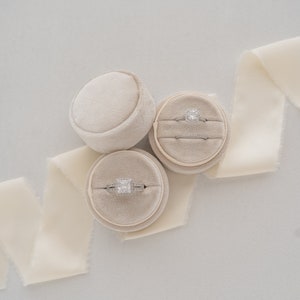 May include: Three beige ring boxes with velvet interiors. Two boxes contain engagement rings with diamonds. One box is empty.