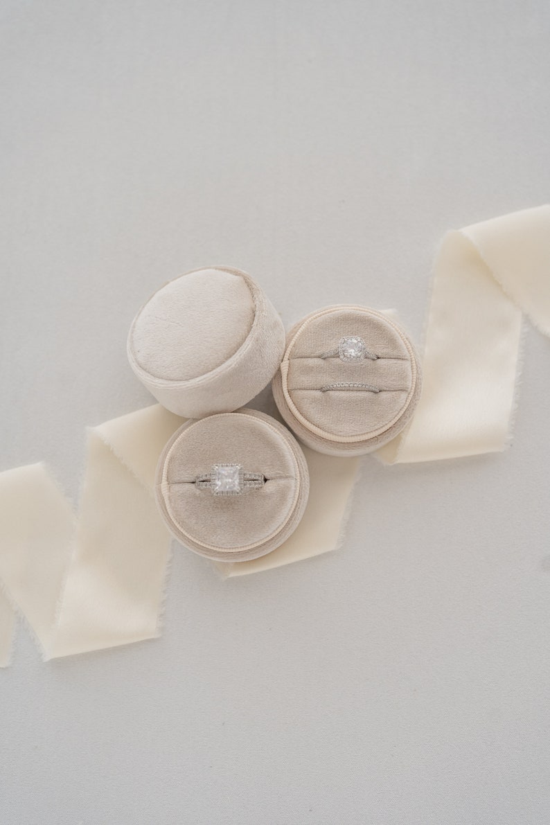 May include: Three beige ring boxes with velvet interiors. Two boxes contain engagement rings with diamonds. One box is empty.