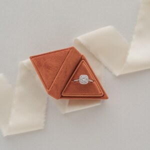 May include: A brown velvet ring box shaped like a pyramid, containing a diamond engagement ring.