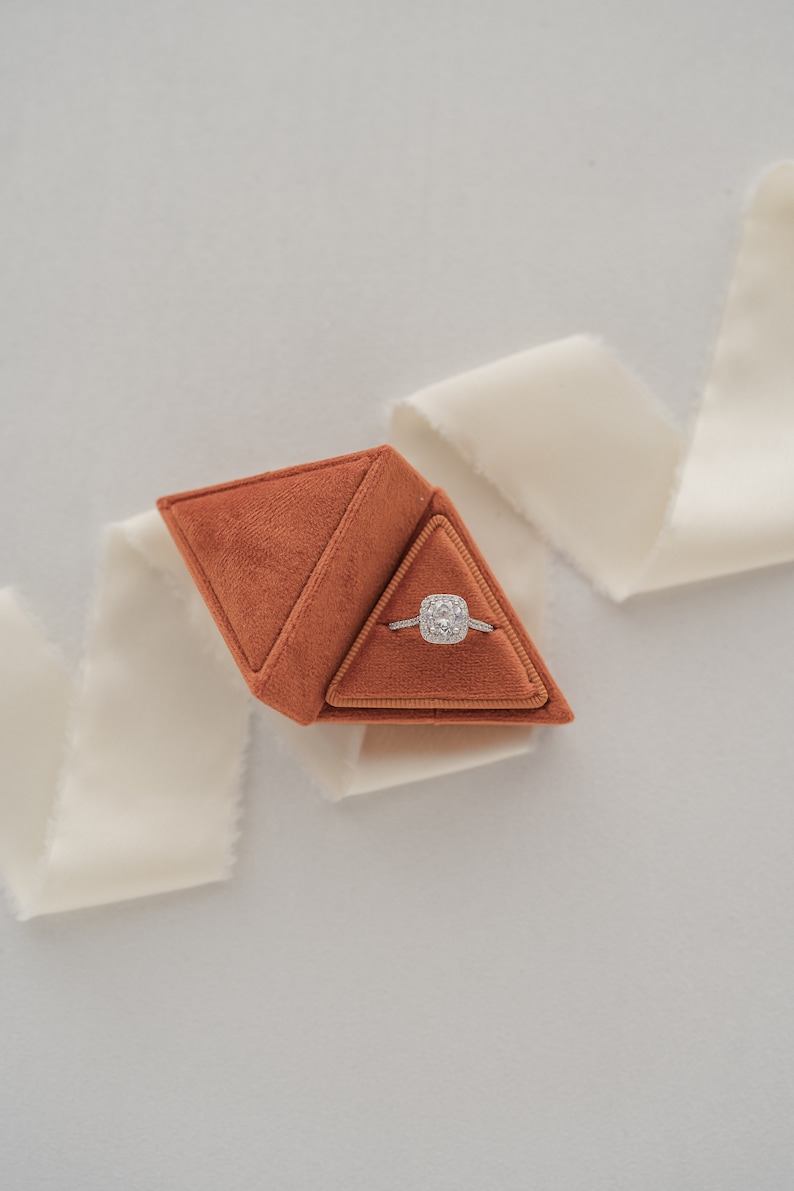 May include: A brown velvet ring box shaped like a pyramid, containing a diamond engagement ring.