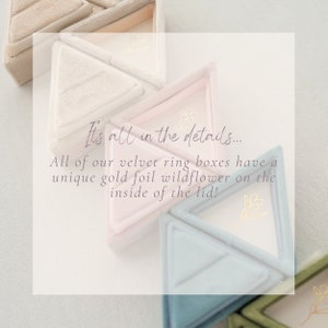 May include: A set of three triangular velvet ring boxes in shades of beige, light pink, and light blue. Each box features a delicate gold foil wildflower design on the inside of the lid. The boxes are arranged in a star shape, with the text "It's all in the details... All of our velvet ring boxes have a unique gold foil wildflower on the inside of the lid!" displayed in front of them.