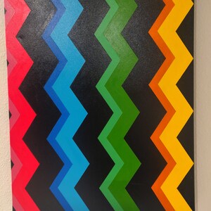 Może przedstawiać: Abstrakcyjny obraz z chevronem w odcieniach czerwieni, błękitu, zieleni, pomarańczy i ż&oacute;łci na czarnym tle.