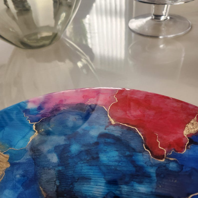 May include: A white ceramic mug with a black handle and the text "But First, Coffee" in a bold, black font. The mug is set against a blurred background, suggesting a cosy setting.