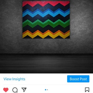 Może przedstawiać: Kolorowy obraz abstrakcyjny z wzorem chevron w odcieniach czerwieni, błękitu, zieleni, ż&oacute;łci i pomarańczy. Obraz wisi na ciemnoszarej ścianie.