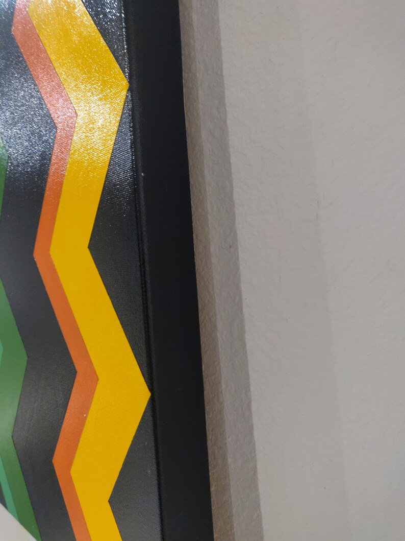 Może przedstawiać: Zbliżenie na kolorowy obraz abstrakcyjny w czarnej ramie. Obraz przedstawia wz&oacute;r w jodełkę w odcieniach zieleni, pomarańczy i ż&oacute;łci.