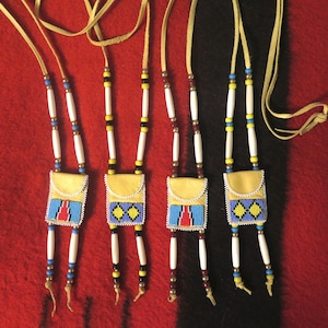 May include: Four beaded leather pouches with colourful beadwork and white bone beads hanging from leather cords. The pouches are decorated with blue, red and yellow geometric patterns.