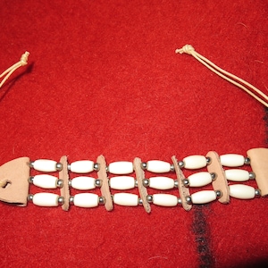 May include: A white bone bead bracelet with leather accents and a tie closure. The bracelet is made of multiple strands of beads and leather.