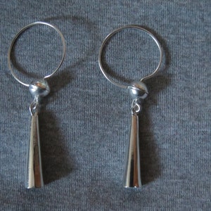 May include: A pair of silver dangle earrings with a round hoop and a cone-shaped pendant.