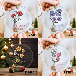 Puede incluir: Adornos navide&ntilde;os de cristal transparente con dise&ntilde;os florales y nombres. Los adornos presentan ilustraciones de flores con nombres como Olivia, Rachelle, Grace y Amelia. Cada adorno tiene una cinta dorada para colgar y texto que indica el mes.